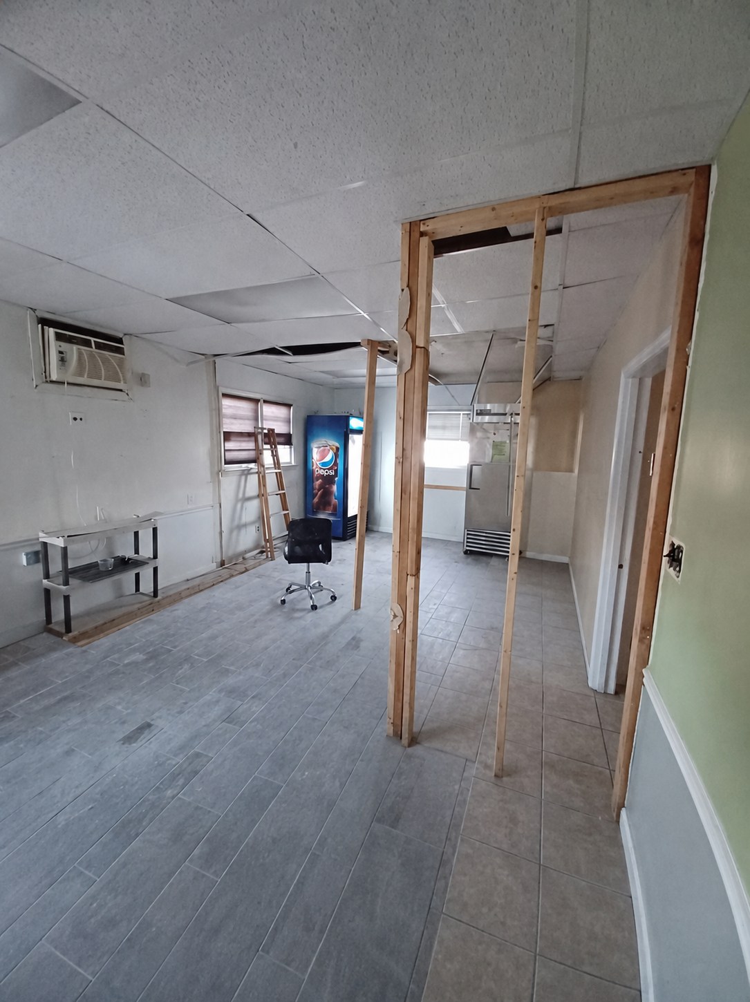 Wide view of the back room with open tiled floor, exposed framing, windows, and display refrigerator